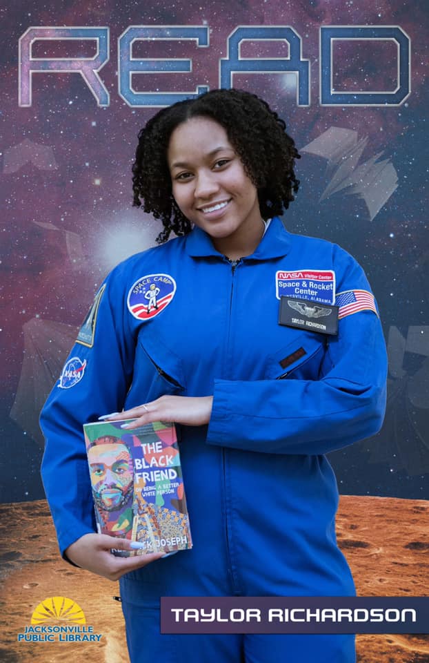Taylor Richardson wearing her space camp suit and holding a copy of The Black Friend Book in her READ poster 
