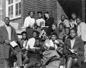 black and white photo of African American students holding books on the step of a school