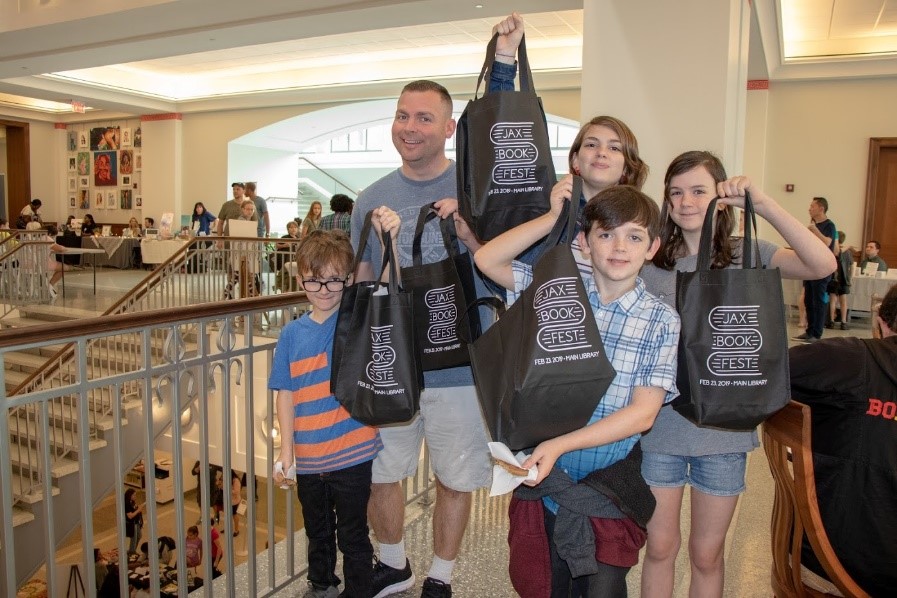 Family holds up tote bags at the Jax Book Fest
