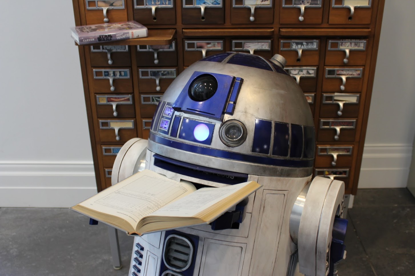 R2-D2 holding a book in front of an old card catalog