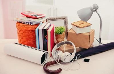 A bunch of random objects on a desk like an umbrella, headphones, books, and a lamp