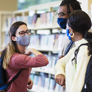 Teens wearing masks greeting each other in the library