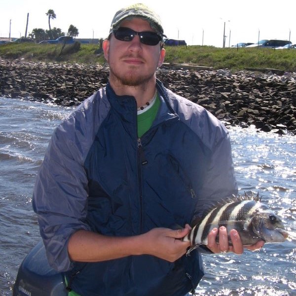 Daniel Powell wearing a hat and sunglasses, holding a fish