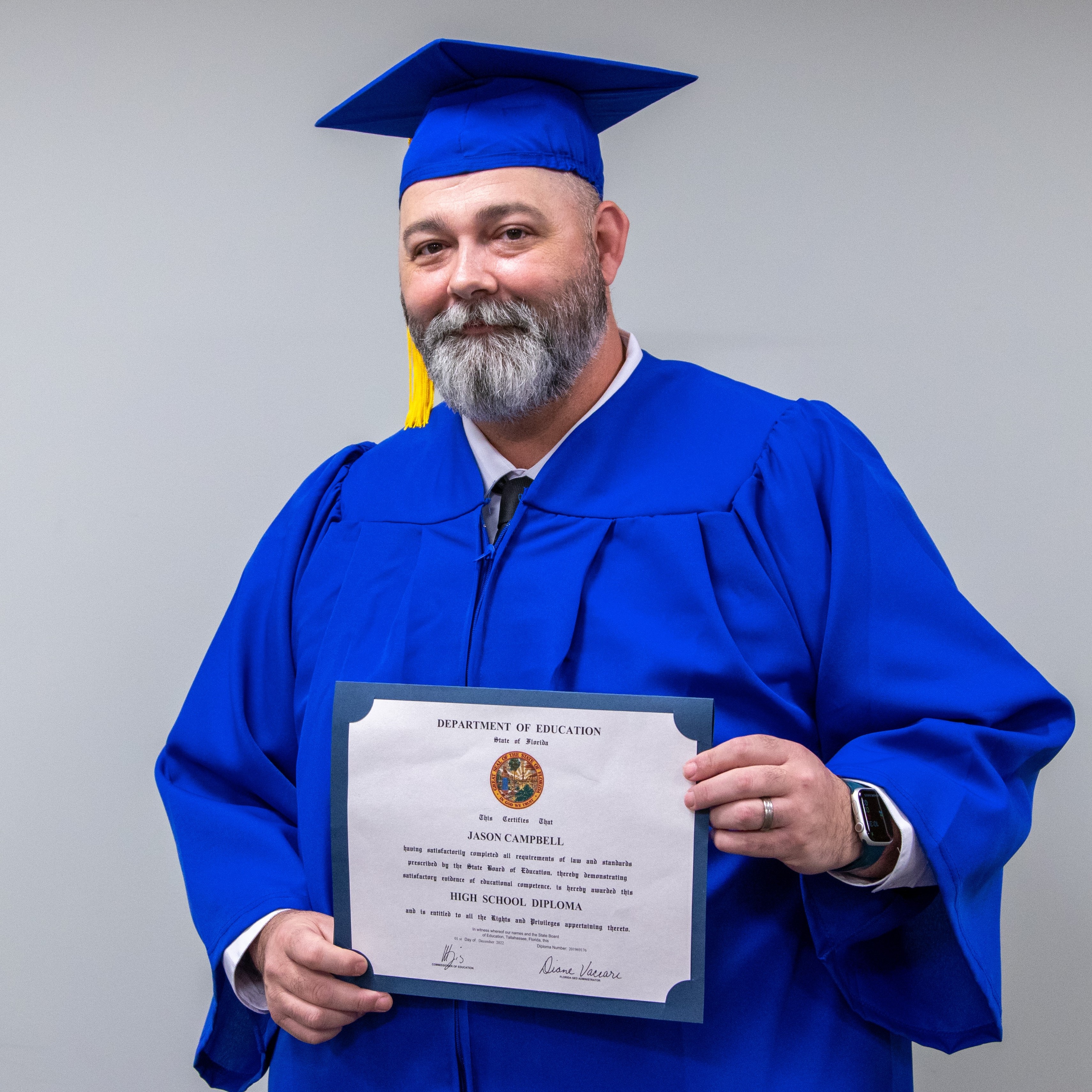 Jason Campbell in a cap and gown, holding his diploma