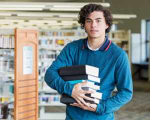 young man holding a stack of books to read he found at the library