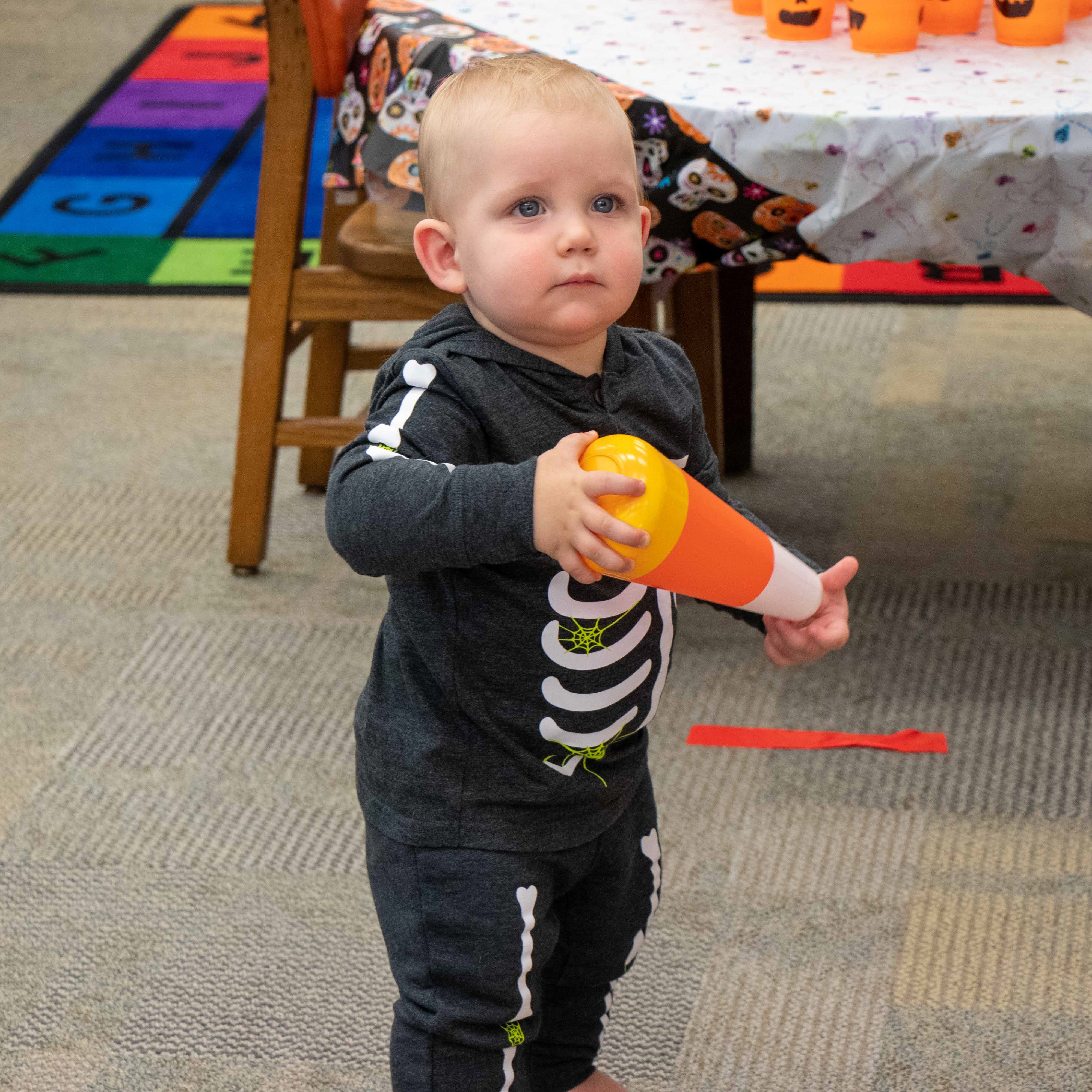 child in a skeleton costume holding a toy candy corn