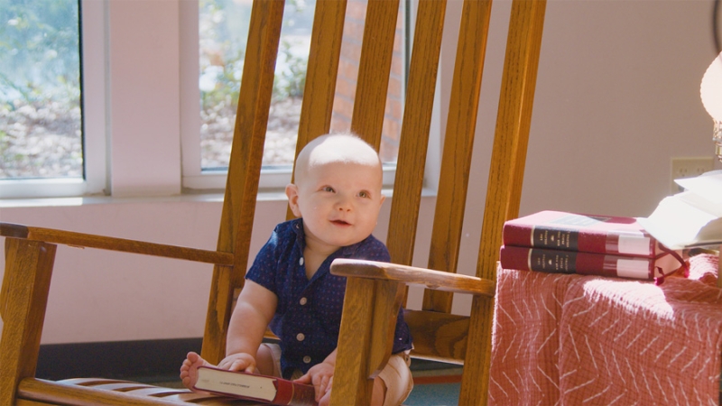 Infant Sitting In Rocking Chair Holding a Library Book