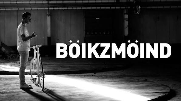 A man stands beside a fixed gear bicycle. The title of the documentary is beside him.