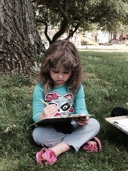 Little girl drawing under a tree