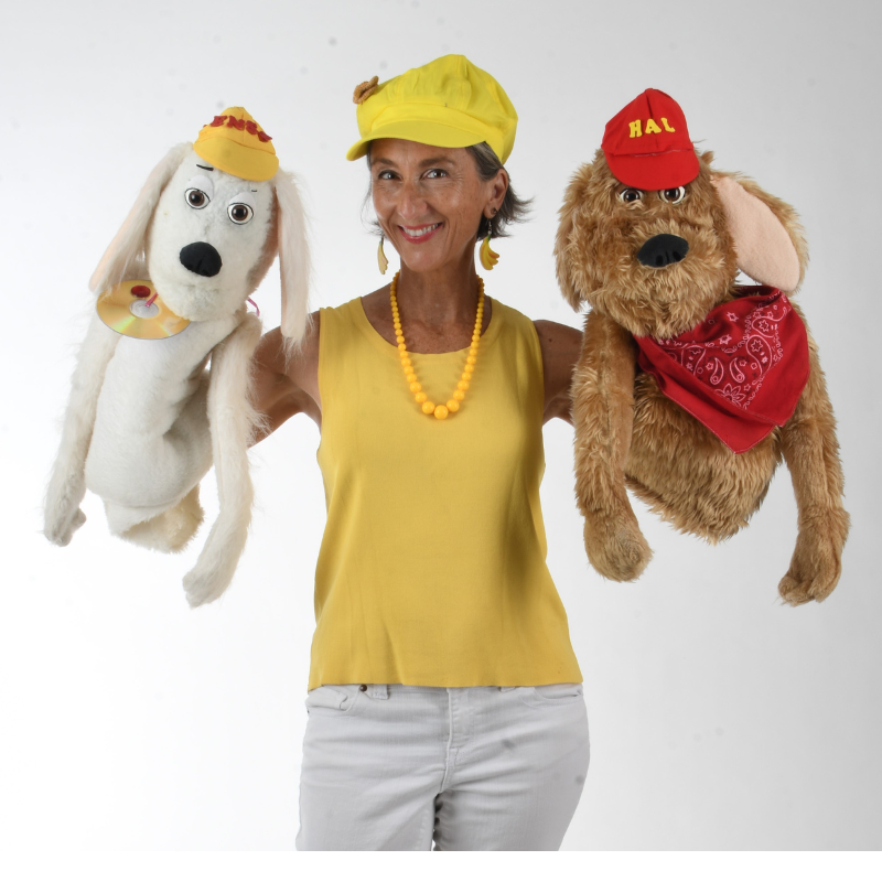 Shana Banana, wearing yellow, and holding two dog puppets