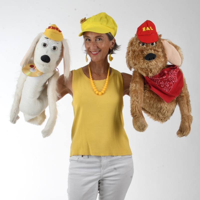 Shana Banana, wearing yellow, and holding two dog puppets