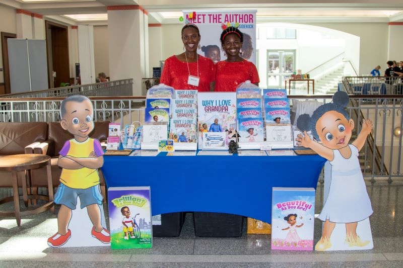 Children's book authors smiling behind a display of their books on a table in the atrium