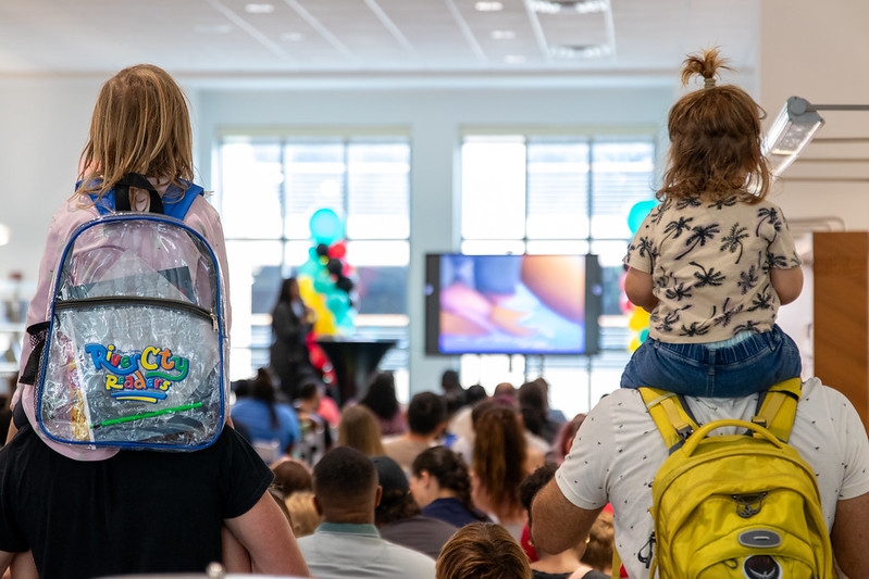 two young girls are being held on the shoulders of their parents, listening to a children's program