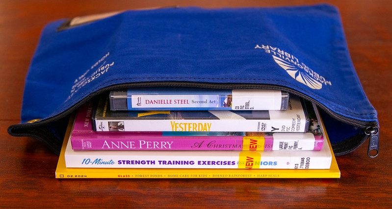 An open, blue bag with a magazine, books and DVDs showing inside 