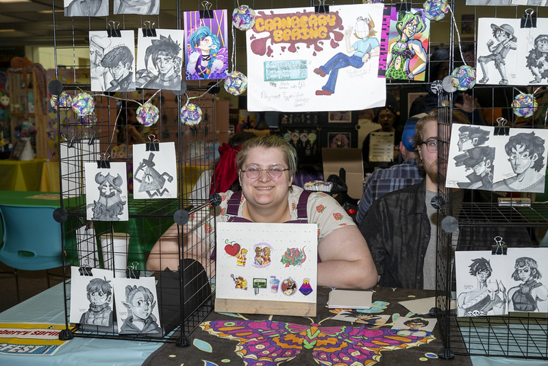 Artist Cranberry Spring at their table, selling prints and keychains