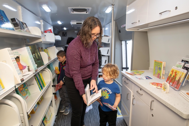 A mother and child look at a book inside the bookmobile