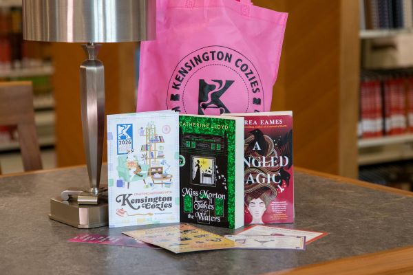 A pink bag with Kensington Cozies logo and several books and other giveaways sitting on a table