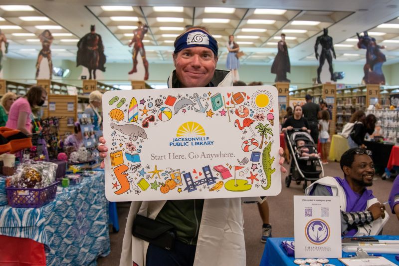 Photo of a man, cosplaying as Naruto, holds an oversized Jacksonville Public Library card