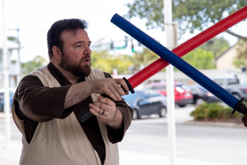 A man dressed as a Jedi imitates combat with a pool noodle light saber.