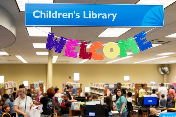 A welcome sign made out of felt hangs from the Children's Library sign. Parents and kids can be seen in the background.