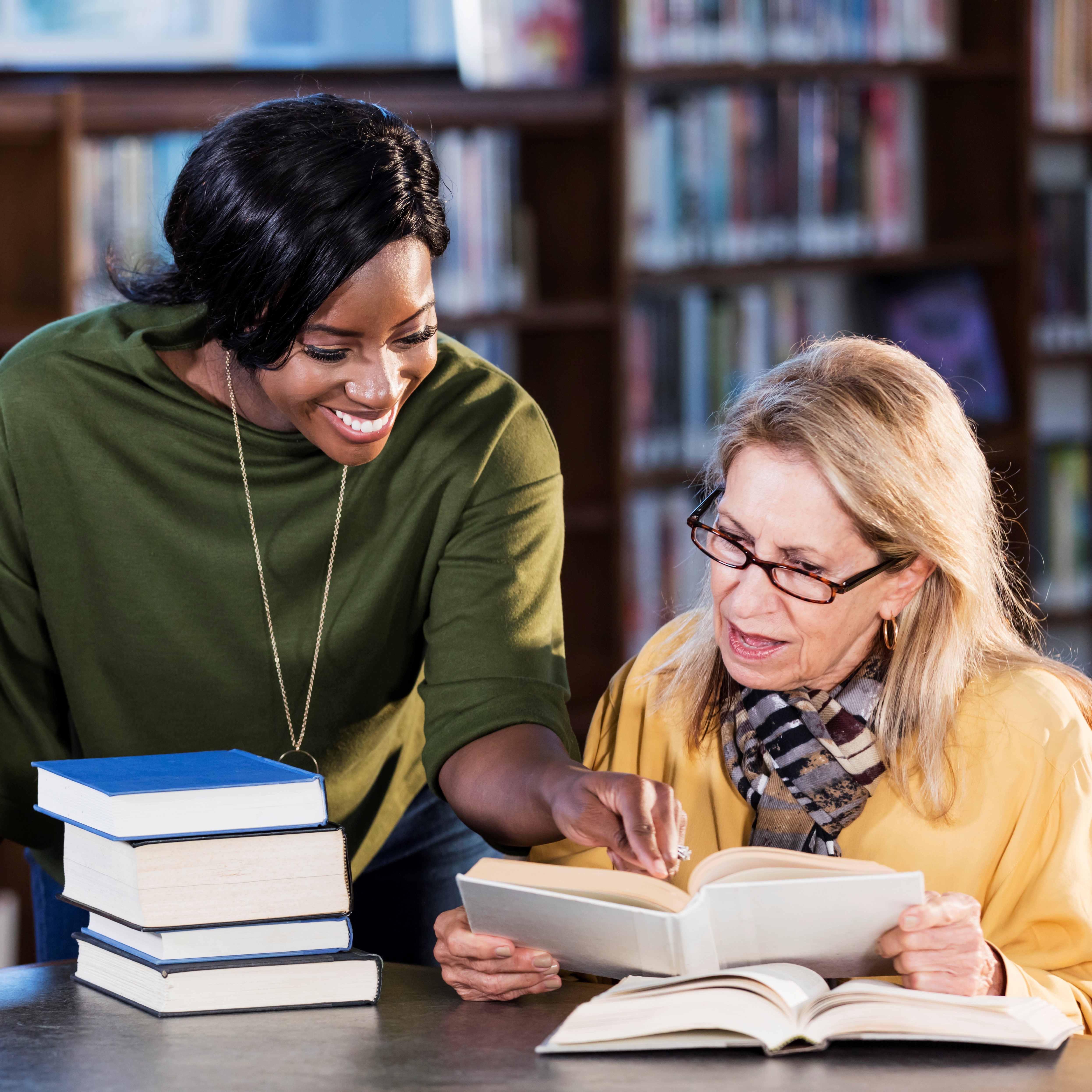 Photo of a women helping another woman find something in a book