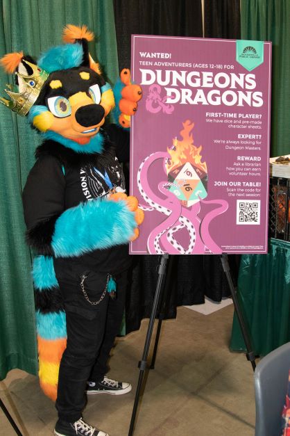 Person in a raccoon fursuit standing by the Library's D&D poster
