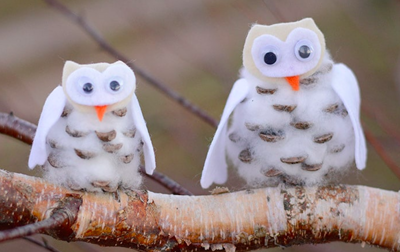 A pair of snowy owls made out of pinecones and craft supplies