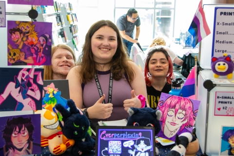 Photo of a vendor with friends. They are surrounded by art prints for sale.