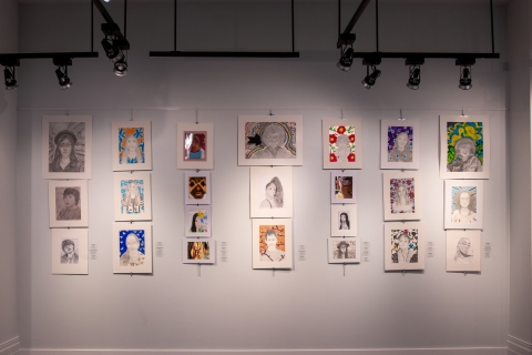 Wide shot of several drawings and paintings hanging on a wall