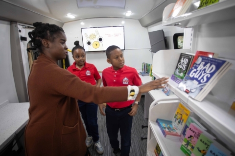 A library staff member showing books to two students inside the bookmobile