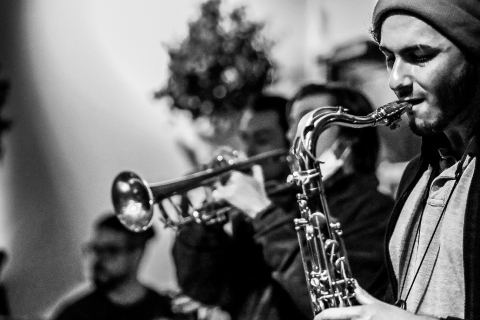 Photo of a man playing a saxophone in the foreground with other musicians in the background