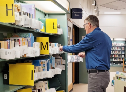 Volunteer man stocks the holds shelf at library