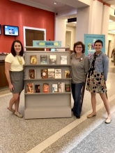 Photo of Jenna, Circe Le Noble and Hurley standing in front of the Great American Read book display at the Main library