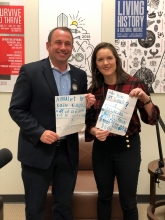 Completely booked podcast host, Jenna posing with Downtown Vision, Inc. CEO Jake Gordon in the Jacksonville Public Library podcast studio. They are holding pieces of paper with blue writings of Jake's kids favorite books