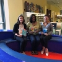 Jenna, Tenikka, and Hurley sitting in the boat in the Main Library Children's department holding children's books