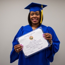 Geneva Barber holds her diploma while wearing a cap and gown