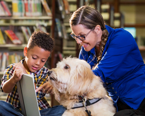 volunteer adult with therapy dog and a child in the library