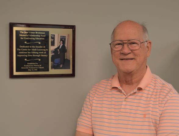 Walter Brinkman standing beside Jean Brinkman's plaque in the Center for Adult Learning